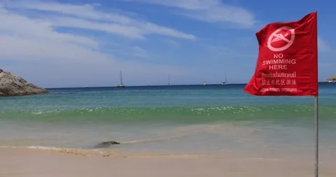 Red «No Swimming here» flag waving in the wind, blue sea waves Andaman Sea Stock Footage 149455094