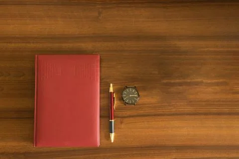 Red notebook with pen and clock on wooden background Foto stock