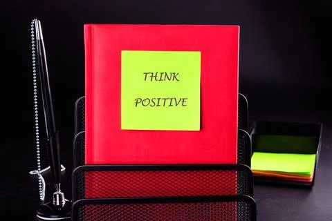 Red notebook stands in a black wire organizer, adorned with a bright yellow note Stock Photos