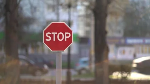 Red octagonal stop sign on metal pole in urban street with blurred cars and Stock Footage 348431187