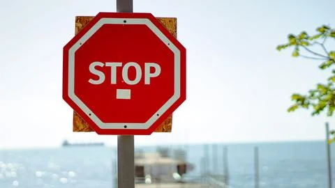 A red octagonal stop sign mounted on a wooden backing near the coast Stock Photos