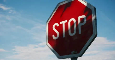 A red octagonal stop sign set against a clear blue sky with tree shadows, c.. Stock Footage 337022991