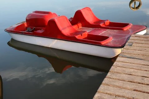 Red paddle boat resting at a dock on a calm lake during the day Stock Photos