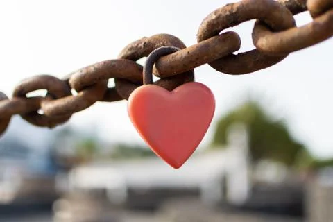 Red padlock in the shape of a heart on a rusty chain Foto stock