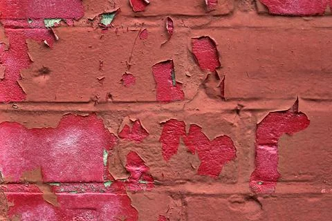 Red paint peeling off over brickwork to reveal pink paint underneath Stock Photos