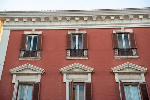 Red painted building facade with classical triangular window pediments, brown Stock Photos