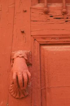 Red painted doorknocker with hand shape on red wooden door Photos