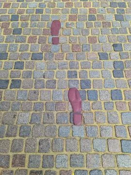 Red painted footprints showing direction on a stone block street Stock Photos