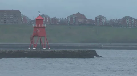 Red painted lighthouse on breakwater in river mouth, choppy waves lap at rocks Stock Footage