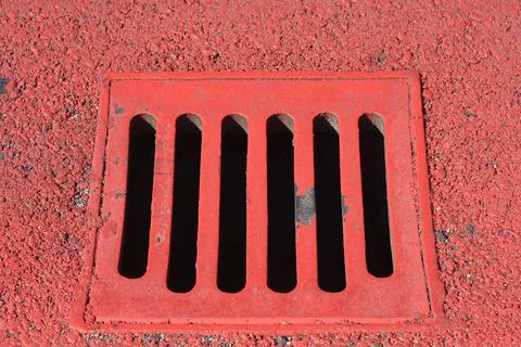 Red painted storm drain grate on textured asphalt surface Stock Photos