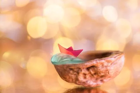 Red paper boat in walnut shell on a shiny gold background Stock Photos