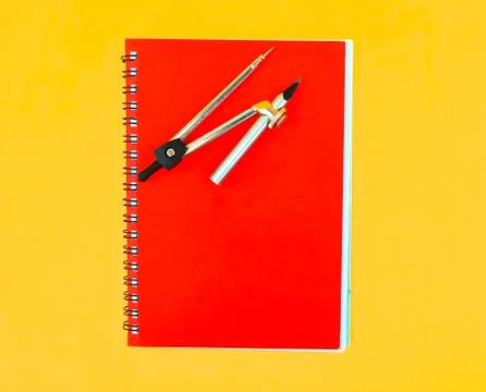A red paper diary placed beneath a compass attached to a silver color pencil Stock Photos