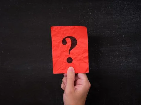 A red paper note with a question mark being held in a hand against a blackboa Stock Photos