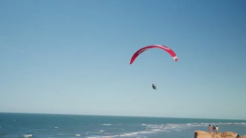 Red Paraglider Flying Over Ocean with Cyclist Watching Video stock 327857059