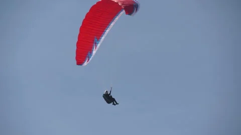 Red paraglider flys through frame against plain pale blue sky background 스톡 동영상 169541277