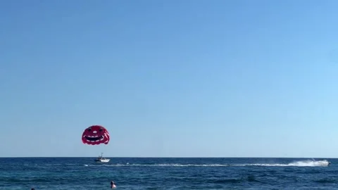 A red paraglider soars above the blue sea with a boat Stock Footage 289965559