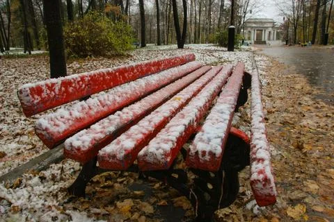 A red park bench, covered in the first snowfall of the season. Stock Photos