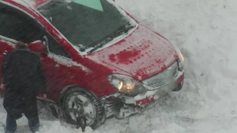 Red passenger car stuck in deep snowdrift during heavy winter snowfall with 스톡 동영상 326751661