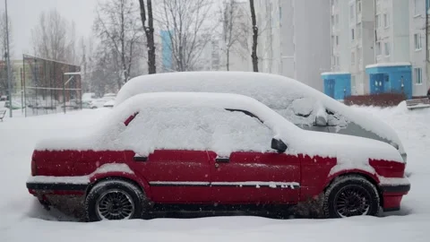 A red passenger car under a cap of snow stands in the yard in winter during a Stock Footage 291779158