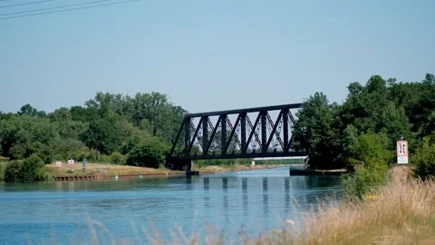 Red passenger regional train crossing a classic steel truss bridge over a w.. Vídeo Stock 337403242