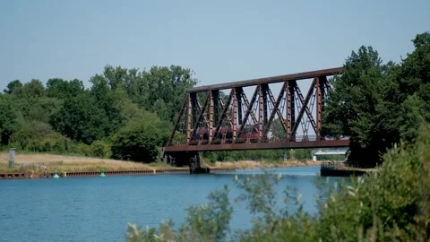 Red passenger train crossing a historic steel truss railway bridge over a w.. Video stock 337404052