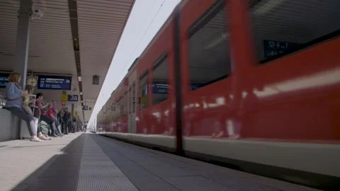Red Passenger Train Departing From Station Platform As Commuters Wait In Sunligh Stock Footage 334055107