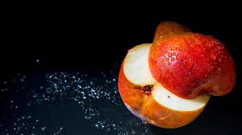 Red pear cut in half with water drops on a black background, close-up, copy s Stock Photos