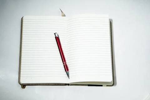 Red pen on open paper notebook on a white background. Stock Photos