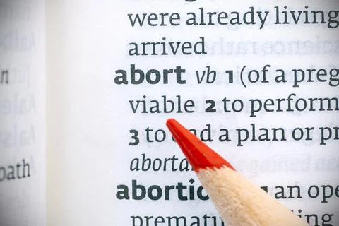 Red pencil on an opened dictionary and abort word, concept picture Stock Photos