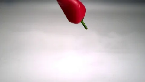 Red pepper chilies falling into clear water and causing a splash in slow motion Stock Footage 81231356