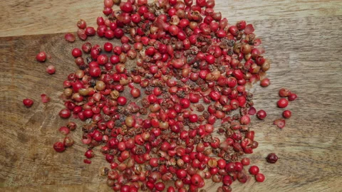 Red peppercorns falling onto a wooden surface and blending together Video stock 233208019