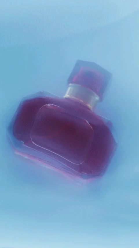 Red perfume bottle placed behind blue translucent fabric veil Stock-Footage 331775161