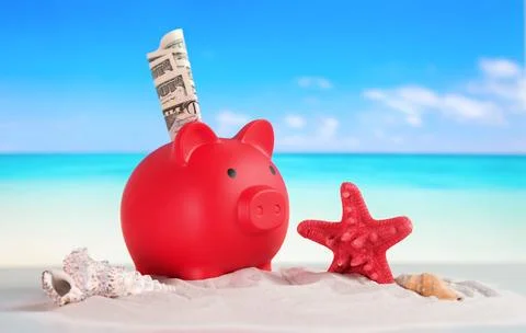 A red piggy bank with a stack of money inside is sitting on a beach Stock Photos