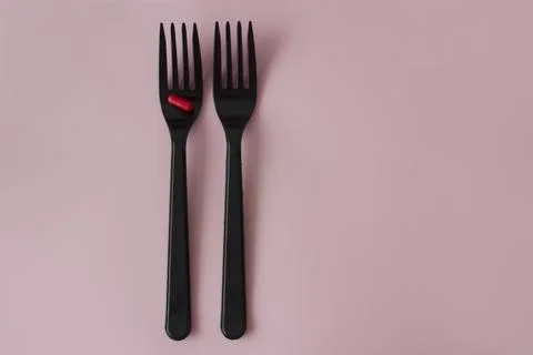 A red pill on a black fork. Two black forks with a red capsule on a pink Stock Photos