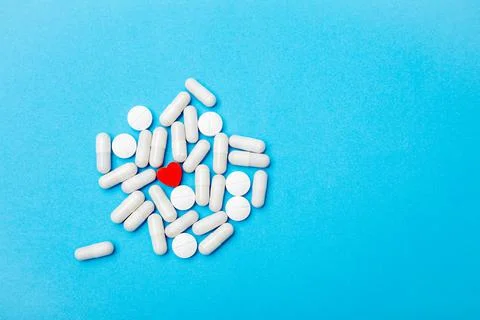 Red pill in the shape of a heart on the background of white pills and a blue Stock Photos