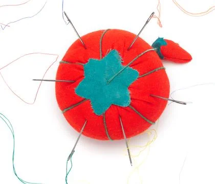 A red pincushion with multiple needles threaded in multicolored yarns, arrang Stock Photos