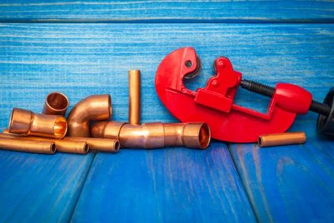 Red pipe cutter and copper pipes with connectors on blue boards Stock Photos