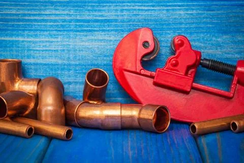 Red pipe cutter and copper pipes with connectors on blue boards Stock Photos