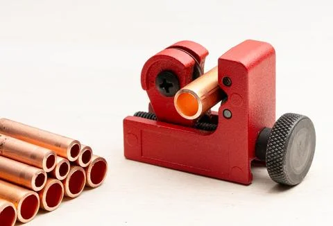 Red pipe cutter tool cutting a copper pipe on a light background Stock Photos