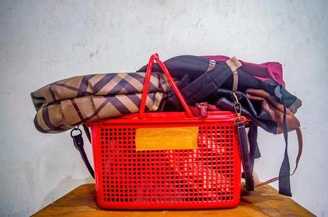 Red plastic basket filled with assorted bags and luggage on a wooden surfac.. Foto stock