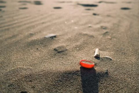 Red plastic bottle cork on sandy sea coast, polluted ecosystem,microplastics Stock Photos