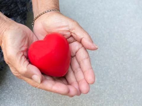 Red plastic heart in the hands of the elderly women. Foto stock