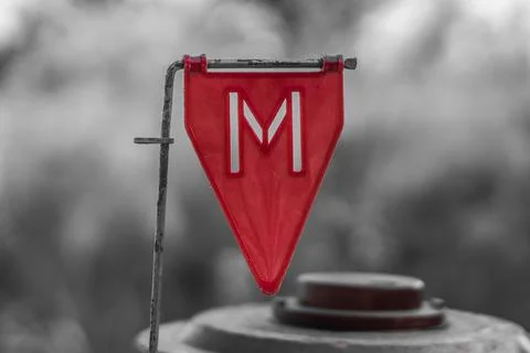 Red plastic minefield pointer "M" with a mine in the background on black and  Stock-Fotos