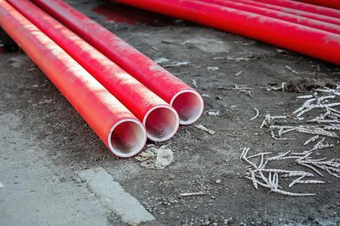 Red plastic pipes, cut into sections, lying on the ground. This juxtapositi.. Stock Photos
