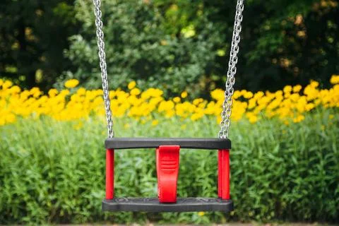 Red plastic swing hanging from chains in a children's park. Stock-Fotos