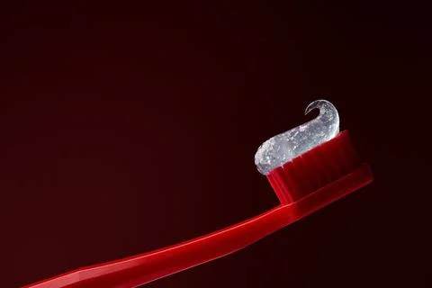 Red plastic toothbrush with transparent toothpaste on a dark red background. Stock Photos