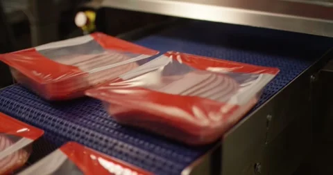 Red plastic trays filled with sliced meat moving along a blue conveyor belt in Vídeo Stock 339992530