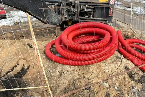Red plastic tubes coiled on construction site during afternoon work near busy Foto stock