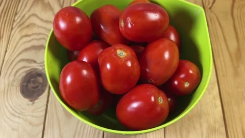 Red plum tomatoes in green plastic bowl on rustic table Stock Footage 346473566