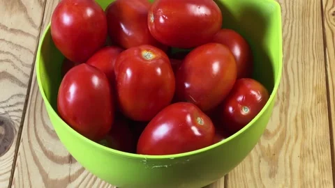 Red plum tomatoes in green plastic bowl on rustic table Stock Footage 346473567